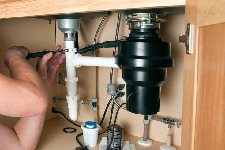 Plumber installing a garbage disposal beneath a kitchen sink in Mableton